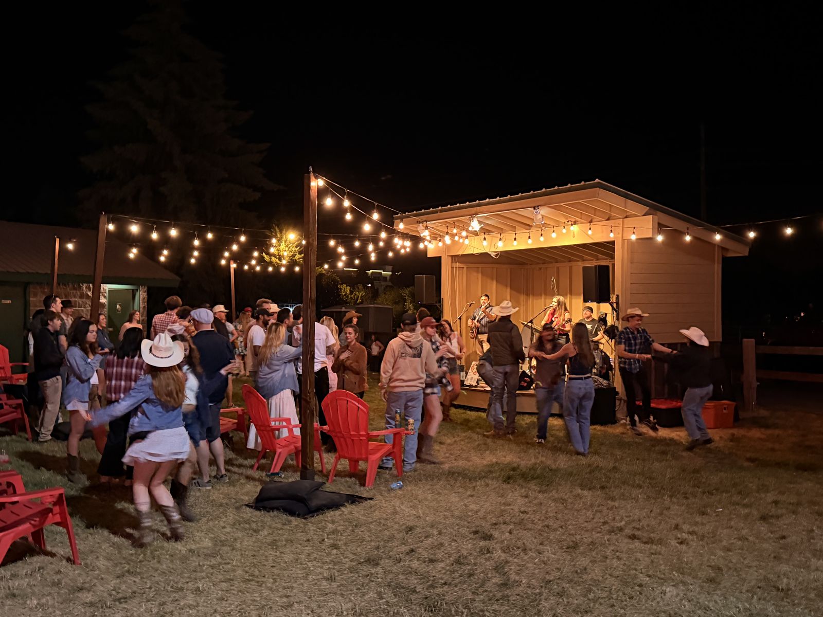 A crowd dancing to a live band on a lit stage under string lights at a Steamboat Pro Rodeo summer night